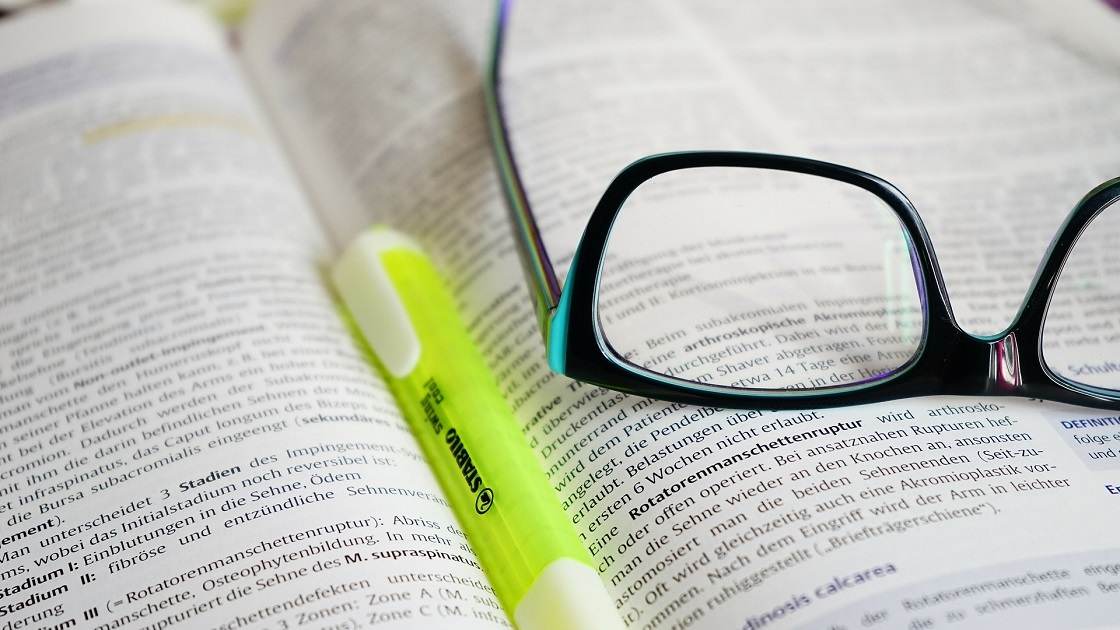 ein aufgeschlagenes wissenschaftliches Lehrbuch und ein Textmarker